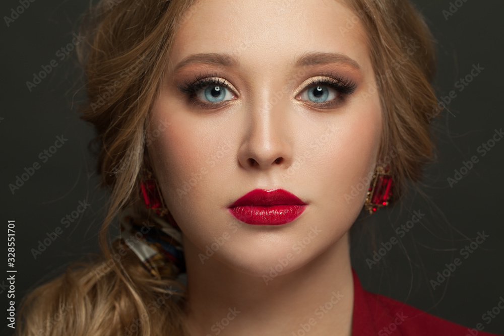 Beautiful woman face with blonde hair, red lips make up and red earrings on black Beautiful woman face with blonde hair, red lips make up and red earrings on black