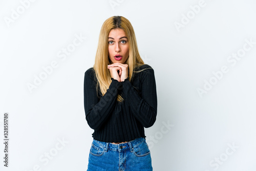 Young blonde woman isolated on white background praying for luck, amazed and opening mouth looking to front.