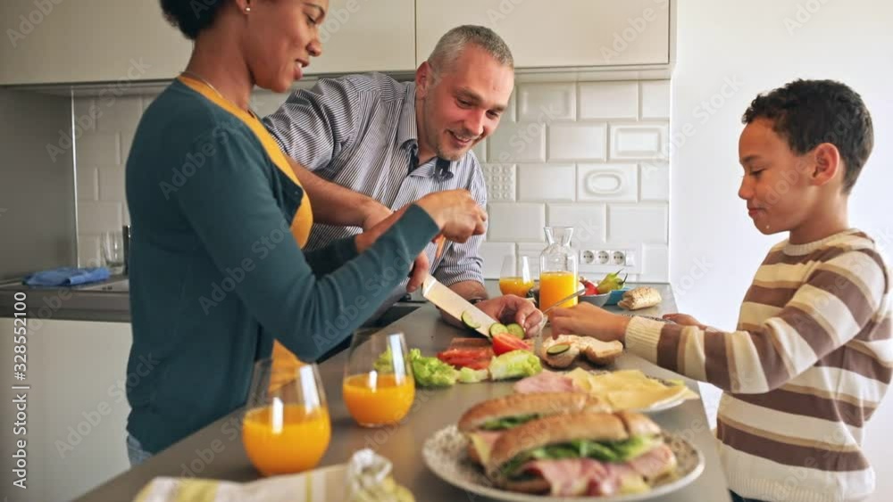 Smiling mixed race family with they son standing in the kitchen preparing sandwich for breakfast at home.