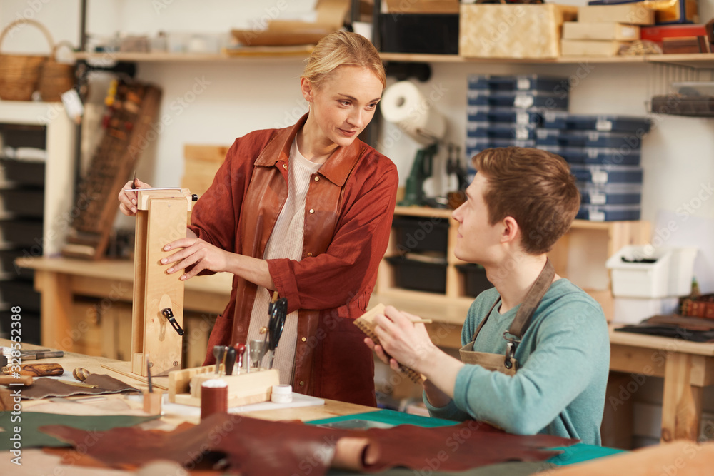 Two young artisans chatting while working together in modern leather craft workshop, horizontal shot Two young artisans chatting while working together in modern leather craft workshop, horizontal shot