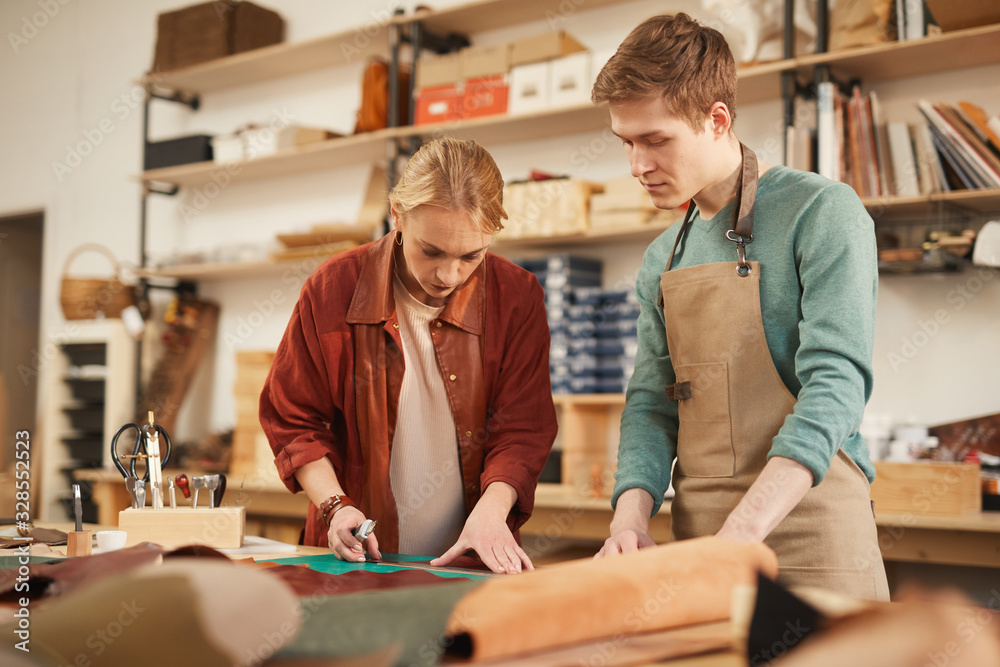 Horizontal medium shot of young Caucasian man and woman working together in modern leather craft workshop Horizontal medium shot of young Caucasian man and woman working together in modern leather craft workshop