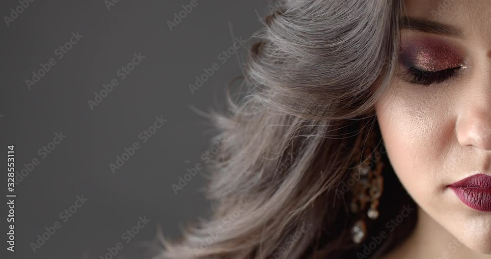 Part of charming woman face with bright eyeshadows and marsala lipstick over dark studio background. Female model with dark curly hair and perfect skin posing on camera. Part of charming woman face with bright eyeshadows and marsala lipstick over dark studio background. Female model with dark curly hair and perfect skin posing on camera.