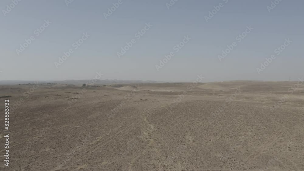 Aerial view of Negev desert landscape, Ezuz village, Israel on the border with Egypt. Hot sunny day. Blue sky. Drone flies above sandy desert land with plants and stones. Aerial view of Negev desert landscape, Ezuz village, Israel on the border with Egypt. Hot sunny day. Blue sky. Drone flies above sandy desert land with plants and stones.