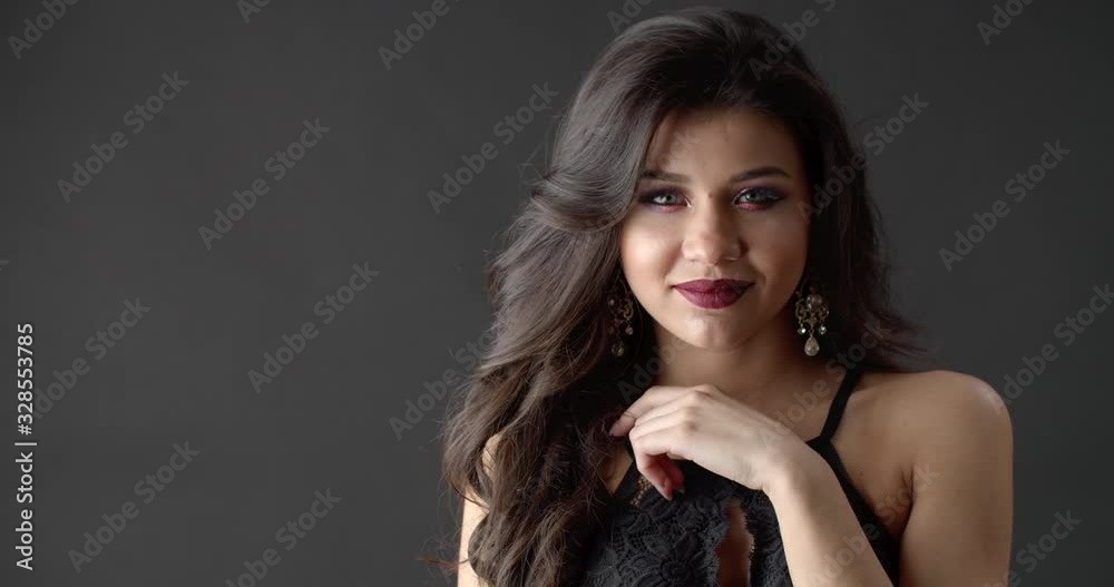 Young brunette woman wearing luxury earrings and black lace underwear working as model on studio with dark background. Professional photoshoot for advertising.
