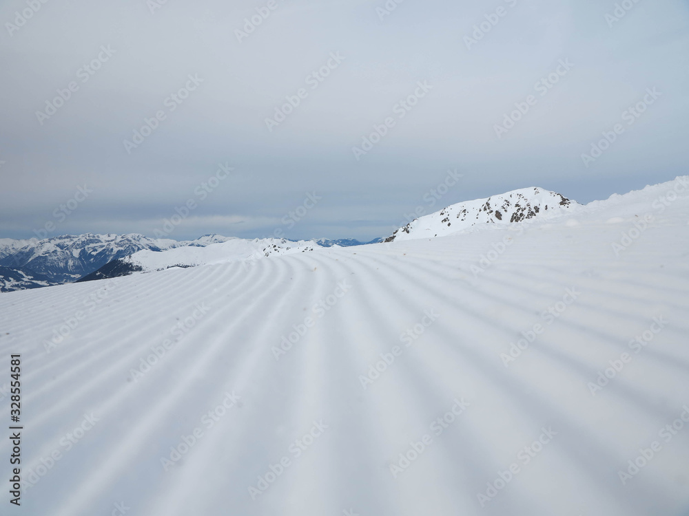 Snow velvet close up on ski slope on the background of snowy mountain peaks. Prepared ski and snowboard track.