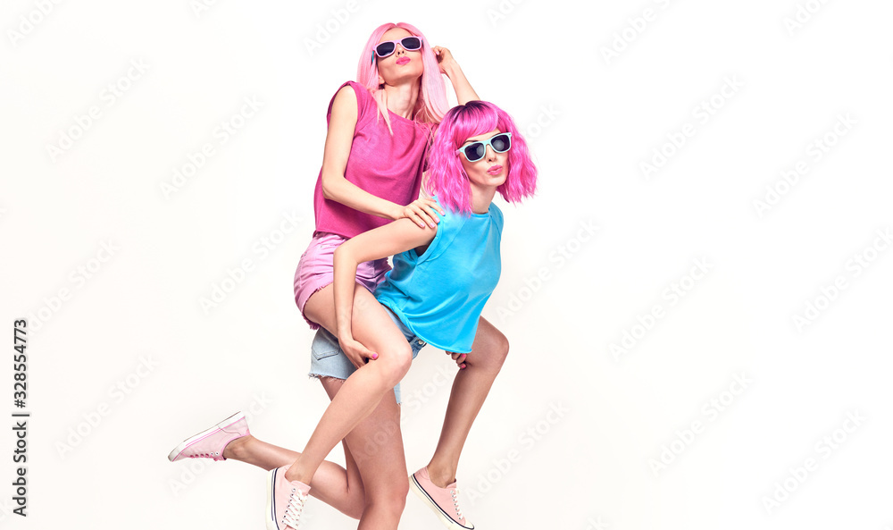 Two fashionable girl having fun in studio. Beautiful Excited young woman in Stylish summer colorful outfit, Trendy dyed pink fashion hair. Funny model sister, pink fashion hairstyle concept on white Two fashionable girl having fun in studio. Beautiful Excited young woman in Stylish summer colorful outfit, Trendy dyed pink fashion hair. Funny model sister, pink fashion hairstyle concept on white