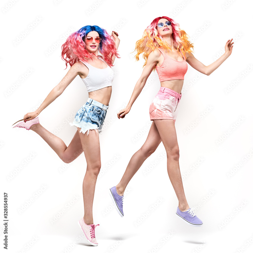 Two Young Woman with stylish pink blue hair, in fashion shorts jump dance. Beautiful fashionable cheerful swag cool girl in summer outfit. Friends with fashion dyed hairstyle jumping on white Two Young Woman with stylish pink blue hair, in fashion shorts jump dance. Beautiful fashionable cheerful swag cool girl in summer outfit. Friends with fashion dyed hairstyle jumping on white