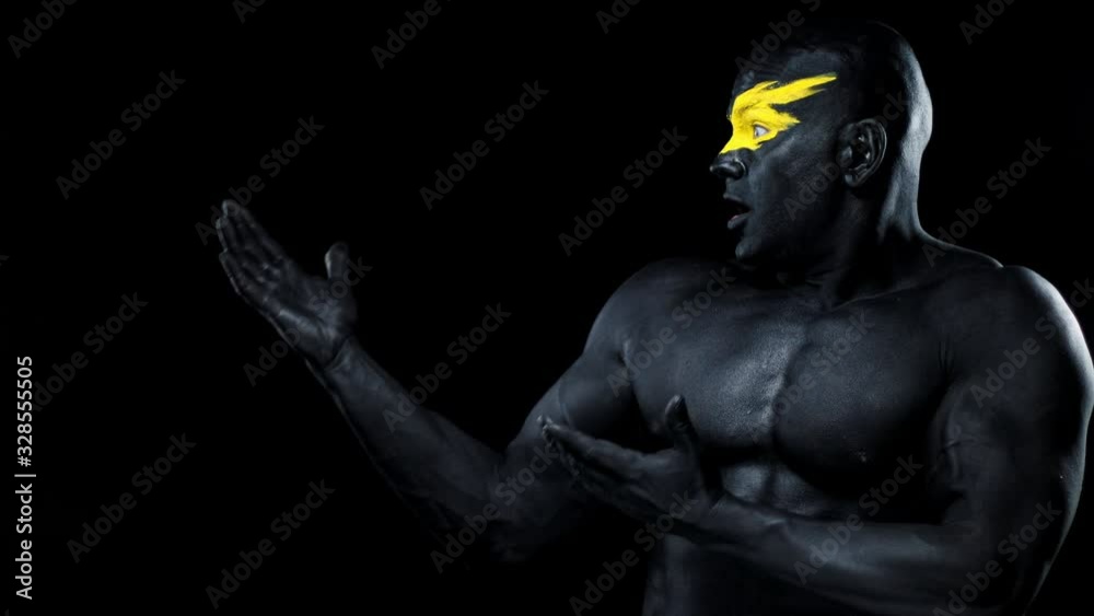 Man with female hands on the body. Bodybuilder athlete with yellow face art and black body paint. Colorful portrait of the guy with bodyart. Man with female hands on the body. Bodybuilder athlete with yellow face art and black body paint. Colorful portrait of the guy with bodyart.