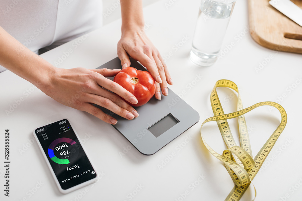 Φωτογραφία cropped view of woman putting tomato on scales near smartphone with calorie coun