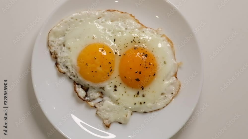 Two fried eggs on plate. Putting plate with fried eggs on wooden table. Close up white porcelain plate with fried egg. Traditional breakfast meal