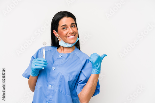 Dentist woman isolated on white background points with thumb finger away  laughing and carefree.