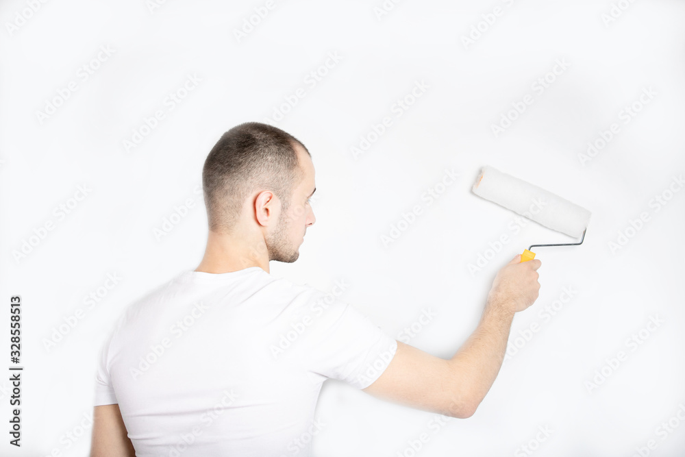 The guy paints the wall with a construction roller. Repair. A handsome young guy. Builder The guy paints the wall with a construction roller. Repair. A handsome young guy. Builder
