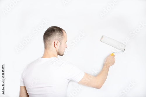 The guy paints the wall with a construction roller. Repair. A handsome young guy. Builder