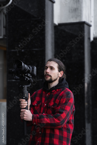 Young Professional videographer holding professional camera on 3-axis gimbal stabilizer. Pro equipment helps to make high quality video without shaking. Cameraman wearing red shirt making a videos.