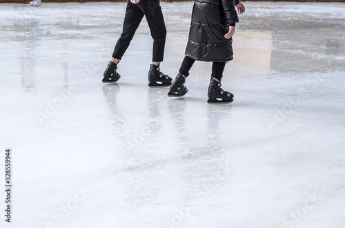 A guy and a girl are skating on an ice rink. Legs close up