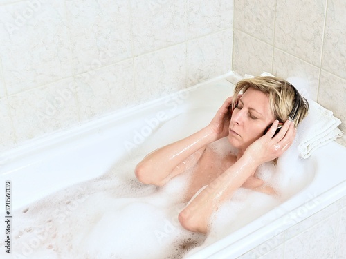 Relaxed woman listening music with headphones in a bubble bath