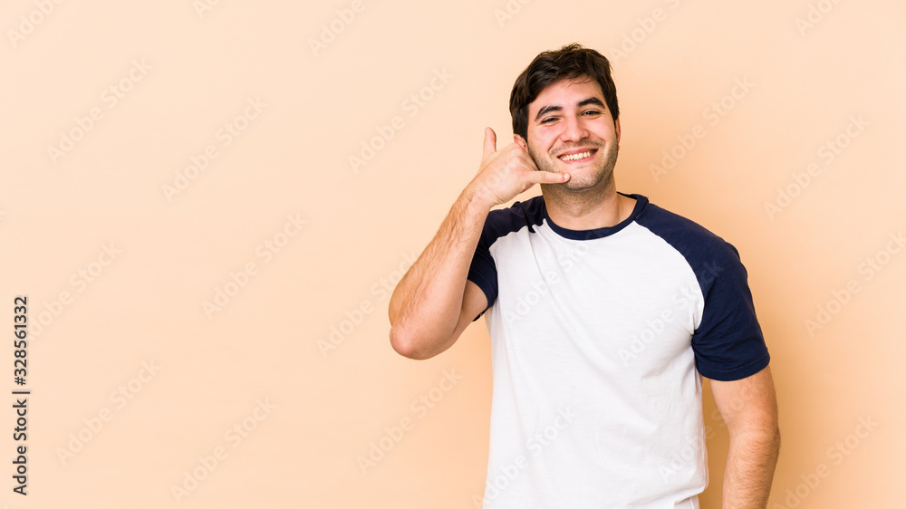 Young man isolated on beige background showing a mobile phone call gesture with fingers. Young man isolated on beige background showing a mobile phone call gesture with fingers.