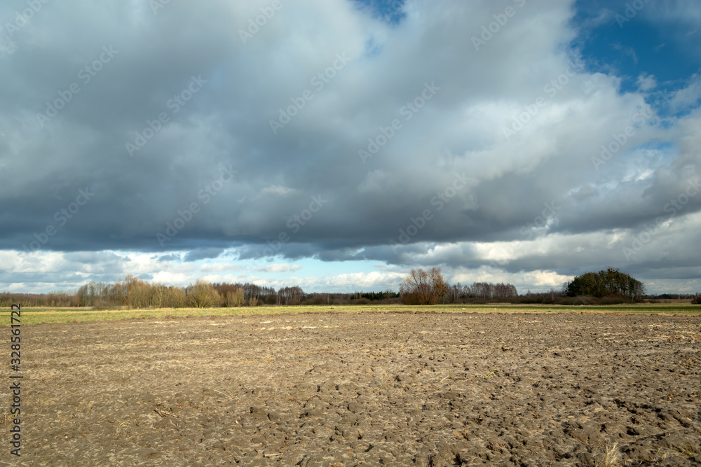 Plowed field and rainy clouds on sky, view on a sunny day