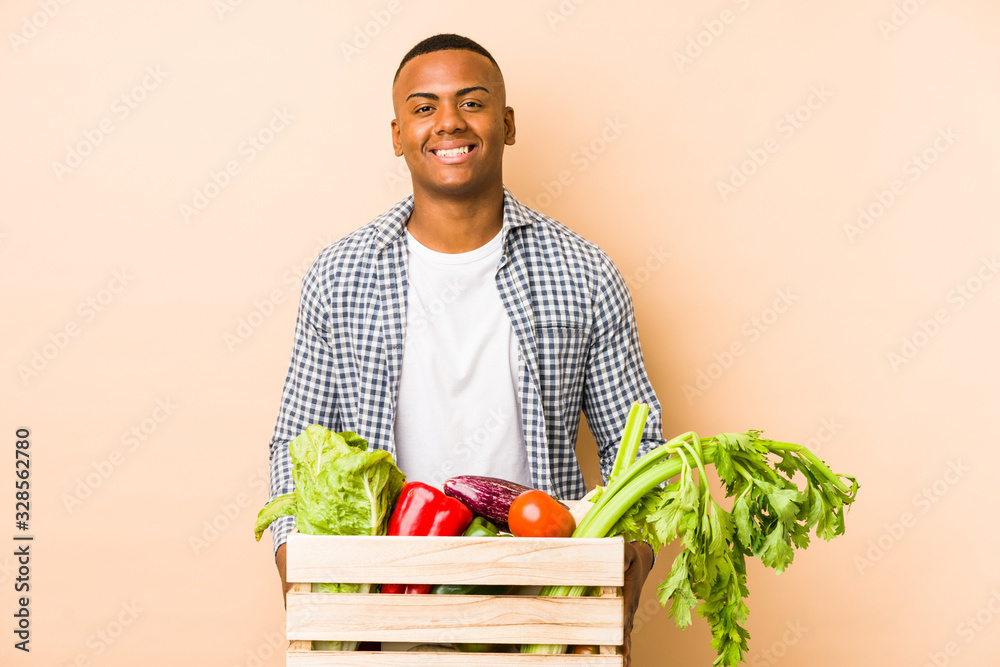 Young farmer man isolated on a beige background happy, smiling and cheerful. Young farmer man isolated on a beige background happy, smiling and cheerful.