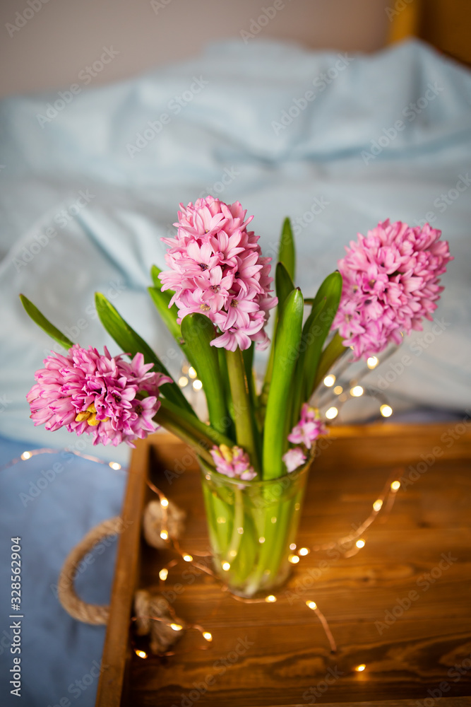 Beautiful pink hyacinths stand in a vase on an old wooden tray, garland, beautiful flickering