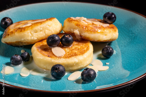 Cheese pancake with almonds and blueberries poured with condensed milk on a blue plate