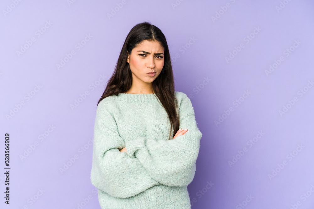 Young indian woman isolated on purple background frowning face in displeasure, keeps arms folded. Young indian woman isolated on purple background frowning face in displeasure, keeps arms folded.
