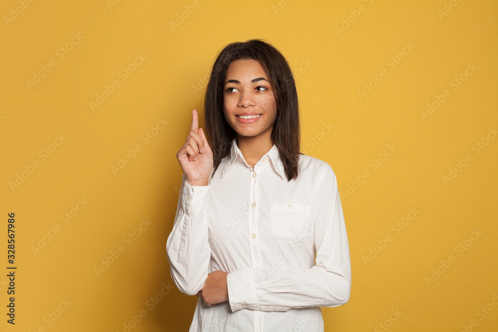 Happy young black woman pointing up on vivid yellow studio background Happy young black woman pointing up on vivid yellow studio background