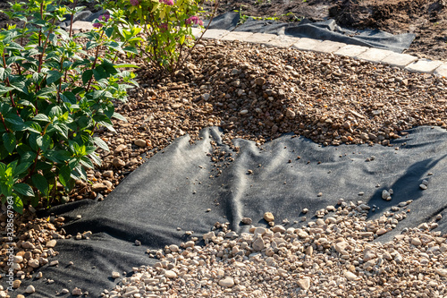 Spreading river pebble over the laid woven geotextile fabric in the summer garden under reconstruction