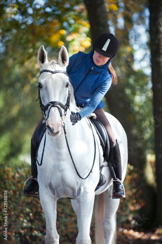 Equestrian lady riding horseback stroking white horse neck