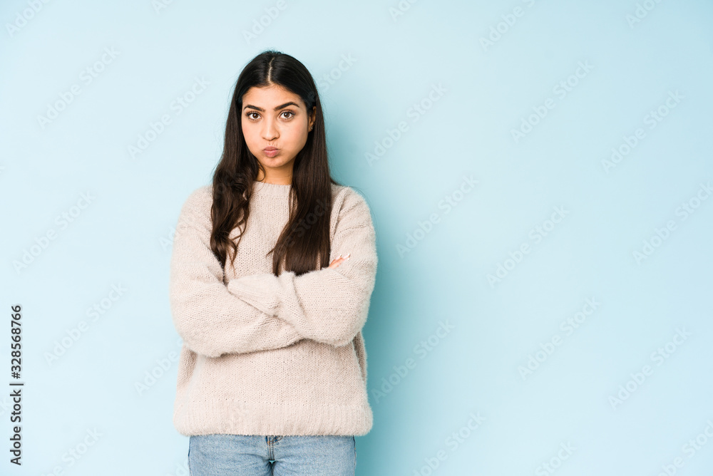 Young indian woman isolated on blue background blows cheeks, has tired expression. Facial expression concept. Young indian woman isolated on blue background blows cheeks, has tired expression. Facial expression concept.