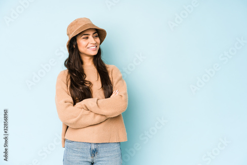 Young indian woman wearing a hat isolated on blue background smiling confident with crossed arms.