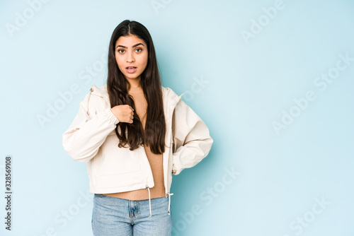 Young indian woman on blue background surprised pointing with finger, smiling broadly. © Asier
