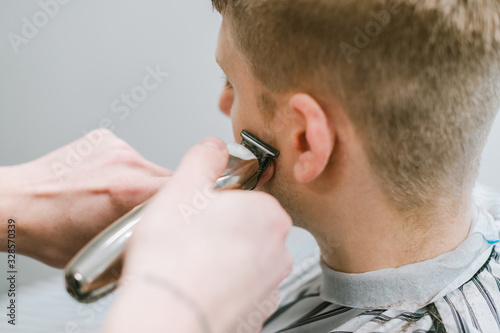 Closeup photo of a male hairdresser trimming client's trimmer. Barbershaw concept. Work of a male hairdresser. Background. Hairdresser cuts hair of blond man.