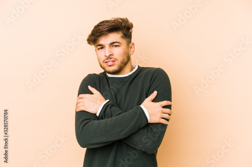 Young arabian man isolated on a beige background going cold due to low temperature or a sickness. © Asier