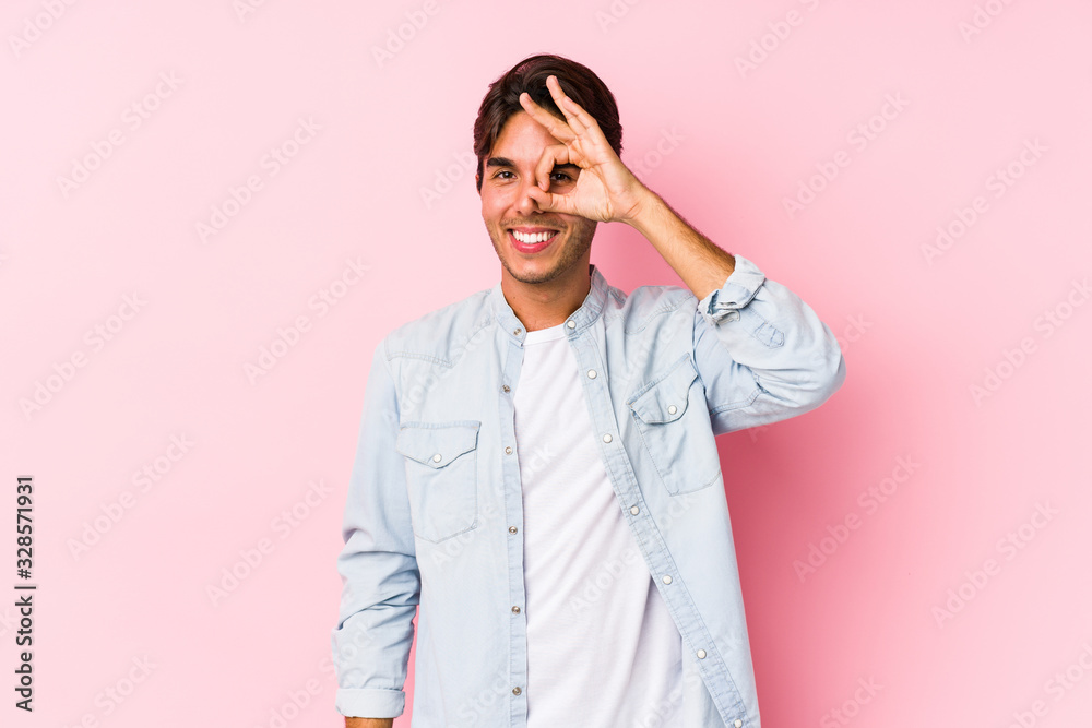 Young caucasian man posing in a pink background isolated excited keeping ok gesture on eye.