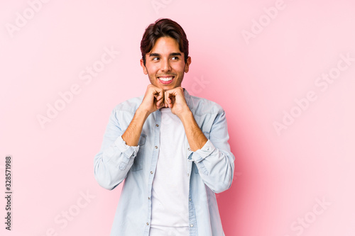 Young caucasian man posing in a pink background isolated keeps hands under chin, is looking happily aside.