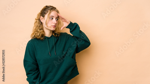 Young caucasian woman isolated on beige background looking far away keeping hand on forehead. © Asier