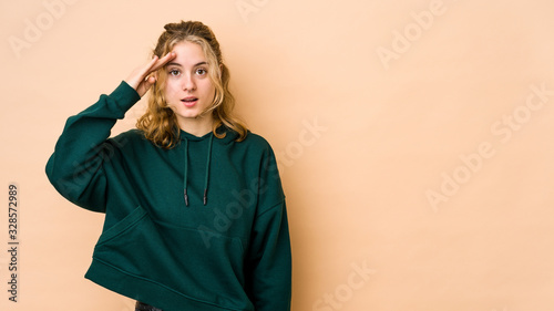Young caucasian woman isolated on beige background shouts loud, keeps eyes opened and hands tense. © Asier