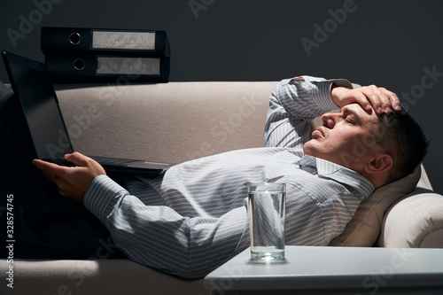 businessman is lying on the sofa with laptop and resting