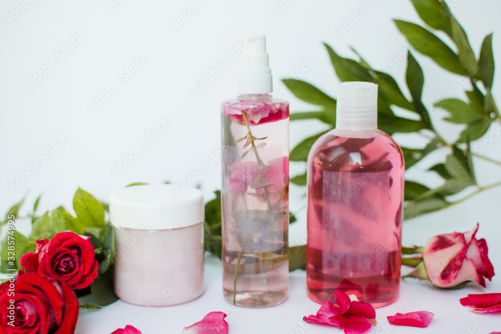 Cosmetic bottles with green leaves and red roses on white background. Natural organic cosmetics Cosmetic bottles with green leaves and red roses on white background. Natural organic cosmetics