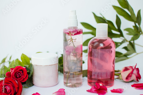 Cosmetic bottles with green leaves and red roses on white background. Natural organic cosmetics