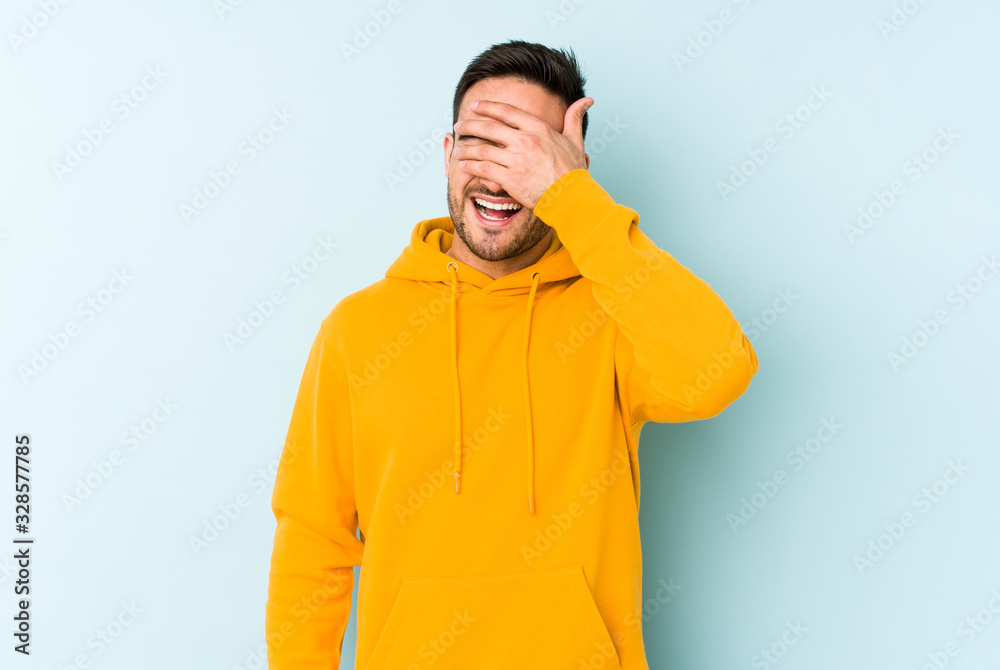 Young caucasian man isolated on blue background covers eyes with hands, smiles broadly waiting for a surprise. Young caucasian man isolated on blue background covers eyes with hands, smiles broadly waiting for a surprise.