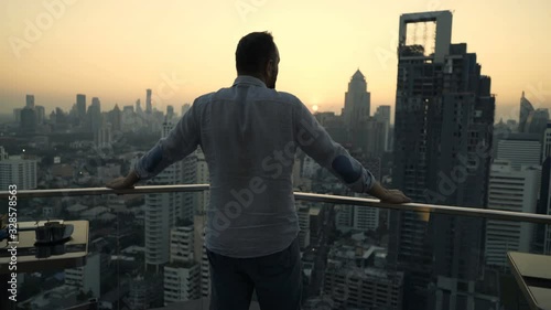 Young man admire beautiful sunset over city at luxury bar
