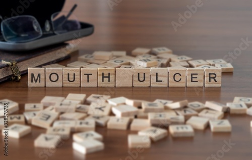 mouth ulcer concept represented by wooden letter tiles on a wooden table with glasses and a book photo