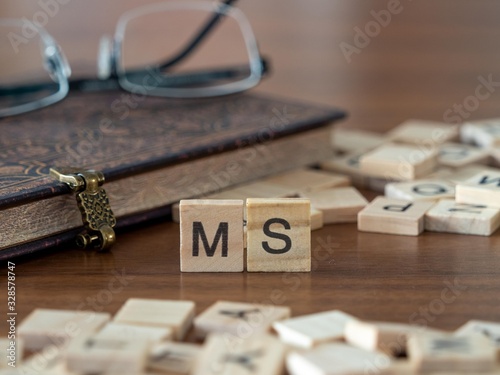 the acronym ms for Multiple sclerosis concept represented by wooden letter tiles on a wooden table with glasses and a book