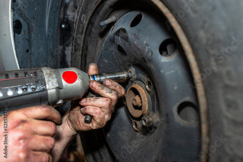 The car mechanic bolts the steel car wheel with a pneumatic wrench in a car workshop, visible male hands.
