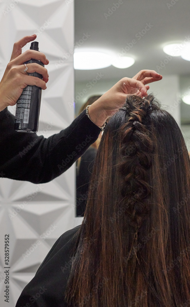 Naklejka premium Hairdresser makes braid and puts hairspray