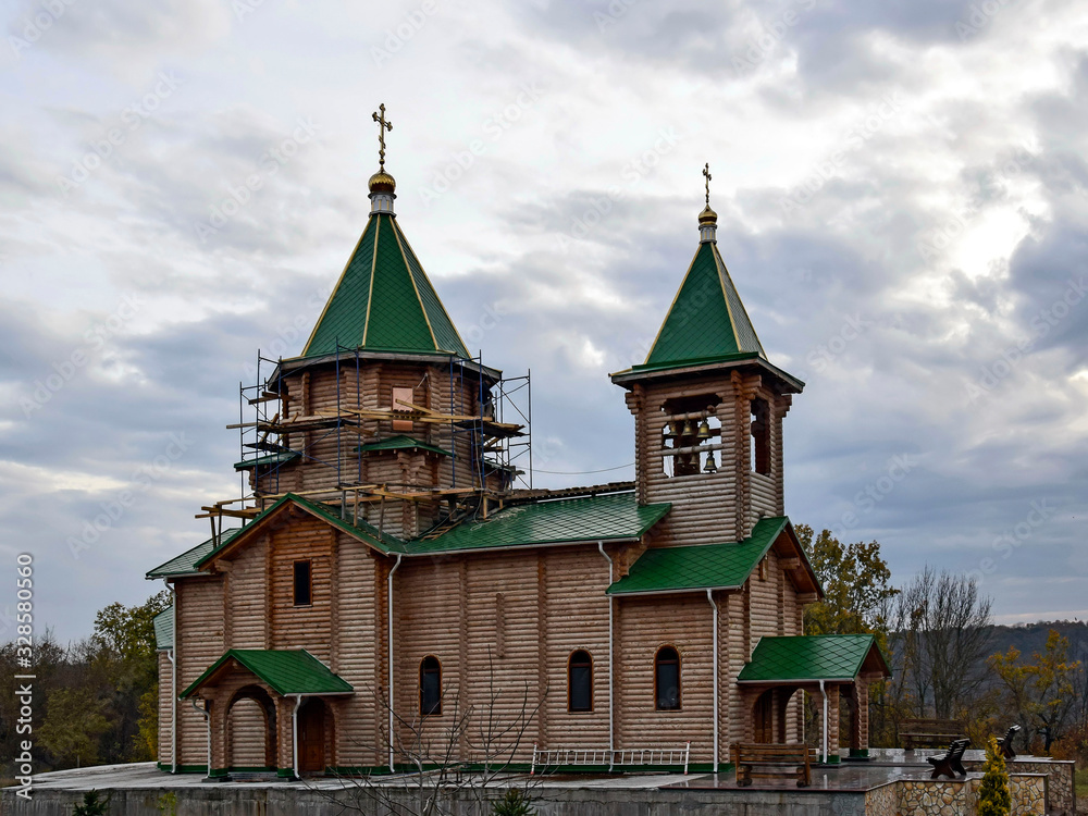 Wooden Orthodox church under construction with green roof and gilded crosses.