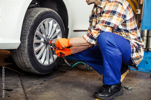 cropped shot of male technician using pneumatic wrench while changing wheel on car