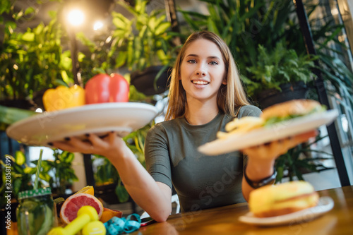 Young beautiful girl making choice between hamburger and a healthy vegetables healthy eating and lifestyle concept photo